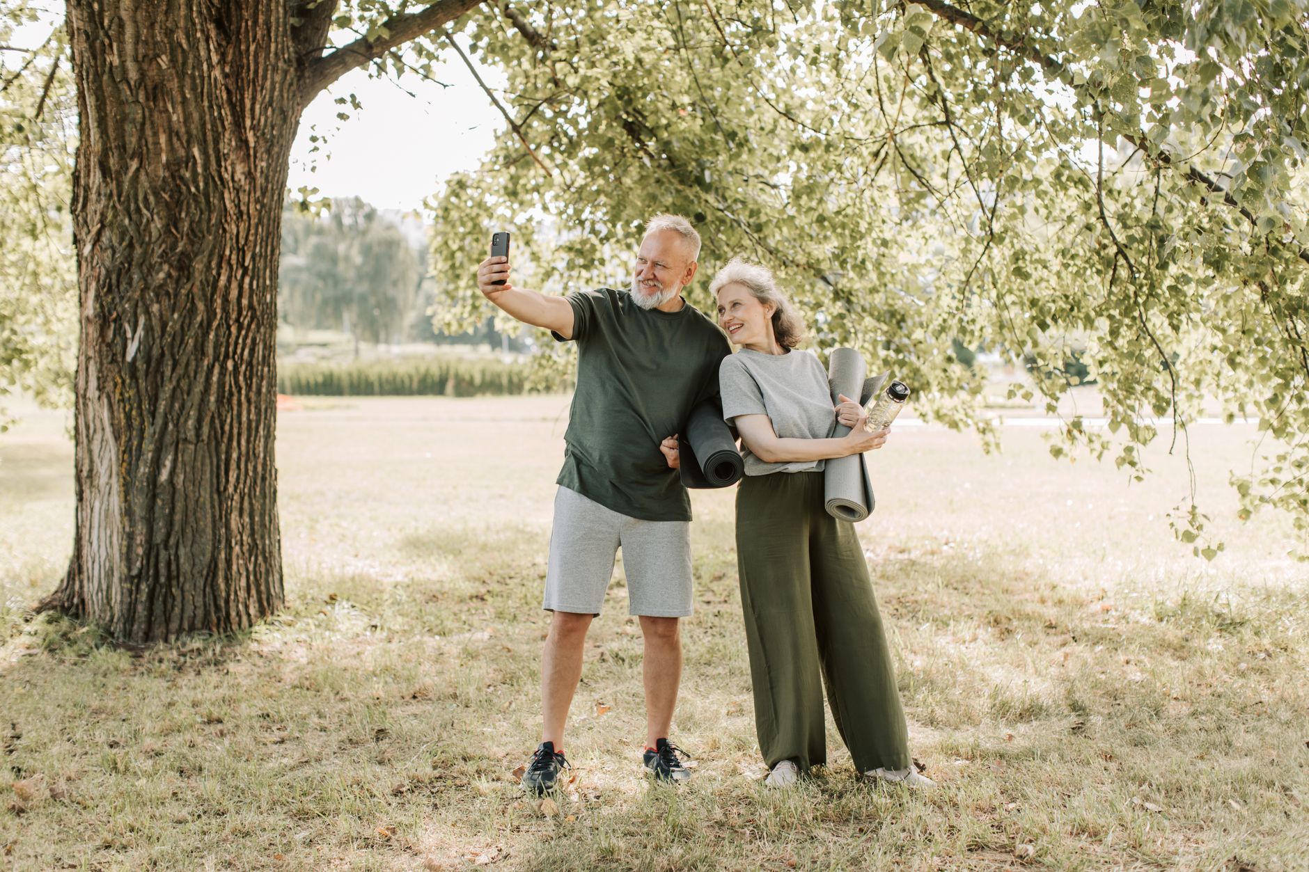 an elderly couple taking selfie while carrying yoga mats